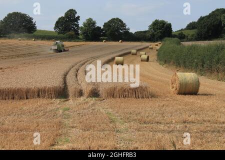 Feld, das am Sommertag in West Yorkshire, Großbritannien, von einem Mähdrescher mit unscharfer Luft und Wolken geerntet wird Stockfoto