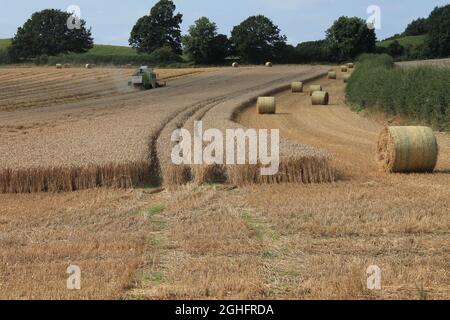 Feld, das am Sommertag in West Yorkshire, Großbritannien, von einem Mähdrescher mit unscharfer Luft und Wolken geerntet wird Stockfoto