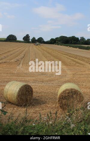 Feld, das am Sommertag in West Yorkshire, Großbritannien, von einem Mähdrescher mit unscharfer Luft und Wolken geerntet wird Stockfoto