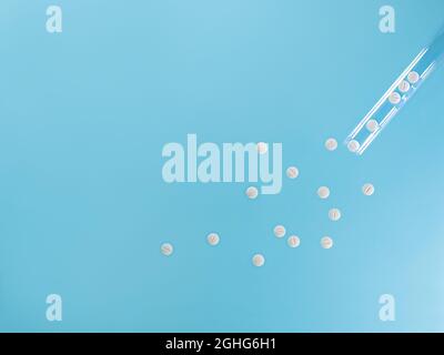 Weiße Pillen aus einem Reagenzglas gegossen. Auf blauem Hintergrund. Stockfoto