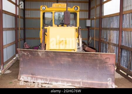 Große leistungsstarke gelbe Traktor mit großen Rädern in den Hangar, Lager, Garage mit offenen Toren Stockfoto