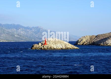 Kleine steinige Insel im Meer mit einem kleinen roten Leuchtturm bei starkem Wind Stockfoto