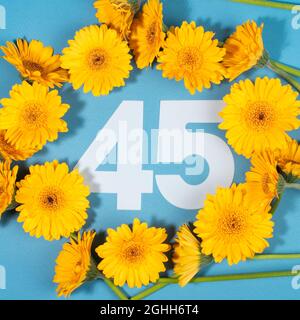 Nummer 45 umgeben von gelben Gerbera-Blüten auf blauem Hintergrund. Stockfoto