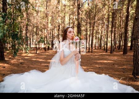 Braut mit weißem Hochzeitskleid im Wald hält bunte und getrocknete Hochzeit Bouquet. . Hochwertige Fotos Stockfoto