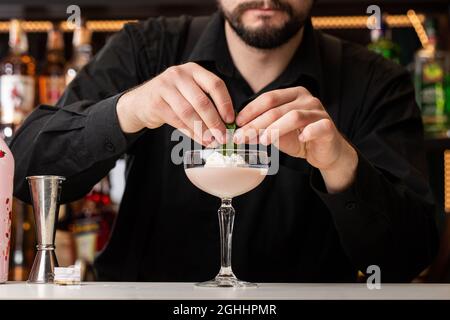 Der männliche Barkeeper schmückt den Cocktail an der Bar mit Eis und Baileys im Glas Stockfoto