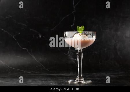 Ein Glas eisgekühlter Baileys-Cocktail, serviert in einem Glas, verziert mit Minzblättern, die auf einem schwarzen Glas platziert sind Stockfoto