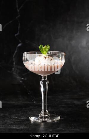 Ein Glas eisgekühlter Baileys-Cocktail, serviert in einem Glas, verziert mit Minzblättern, die auf einem schwarzen Glas platziert sind Stockfoto