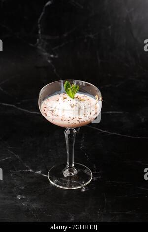 Ein Glas eisgekühlter Baileys-Cocktail, serviert in einem Glas, verziert mit Minzblättern, die auf einem schwarzen Glas platziert sind Stockfoto