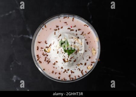 Ein Glas eisgekühlter Baileys-Cocktail, serviert in einem Glas, verziert mit Minzblättern, die auf einem schwarzen Glas platziert sind Stockfoto