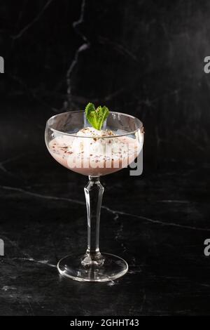 Ein Glas eisgekühlter Baileys-Cocktail, serviert in einem Glas, verziert mit Minzblättern, die auf einem schwarzen Glas platziert sind Stockfoto