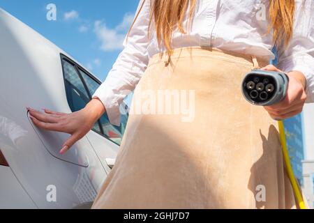 Nahaufnahme einer kaukasischen Frau, die eine Ladesteckdose für Elektroautos öffnet und ein Ladegerät einsteckt Stockfoto