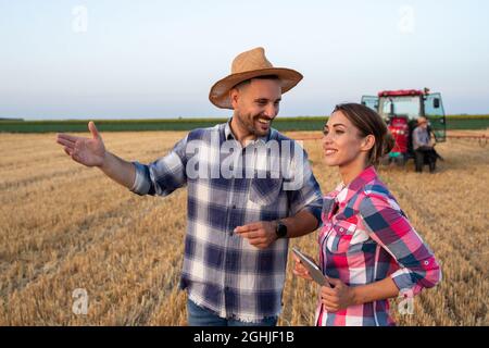 Zwei Bauern, Mann und Frau, die während der Ernte auf dem Weizenfeld mit Traktor im Hintergrund im Sommer sprechen Stockfoto