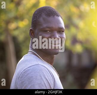 Porträt eines lächelnden und zufriedenen jungen afrikanischen Mannes, der im Park steht Stockfoto