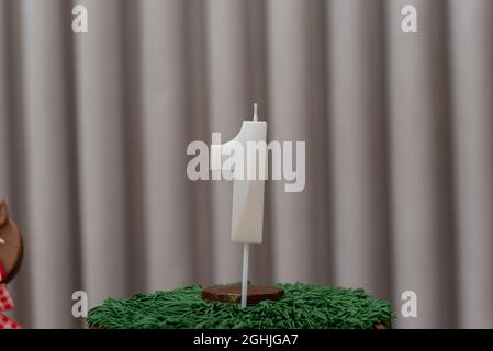 Weiße Kerze in Form der Nummer eins in Schokoladenkuchenvereisung. Festlichkeit, 1 Jahr Jubiläum und Wachstumskonzept. Stockfoto