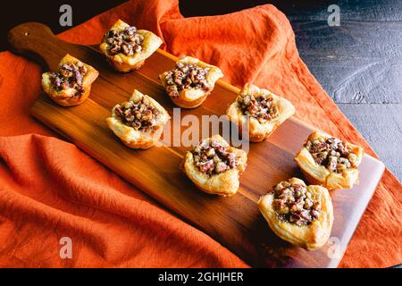 Pecan Pie Tartelettes serviert auf einem Holzschneidebrett: Einzelne Pecan Pie Tarteletten werden auf einem Holzschneidebrett angezeigt Stockfoto