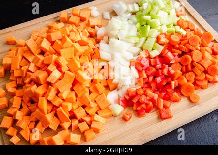 Gehacktes Gemüse auf einem Bambusschneidebrett: Geschälte und gewürfelte Süßkartoffeln, Zwiebeln, Sellerie, Karotten und rote Paprika auf einem Holzschneidebrett Stockfoto