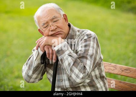 Einsamer älterer Mann, der auf der Parkbank sitzt Stockfoto