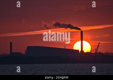 Teleansicht des epischen orangen Sonnenuntergangs über dem Hafen von Dublin und der Sonne, die mit dem Werk Covanta (Dublin Waste to Energy) in Einklang steht, vom westlichen Pier von Dun Laoghaire aus gesehen Stockfoto