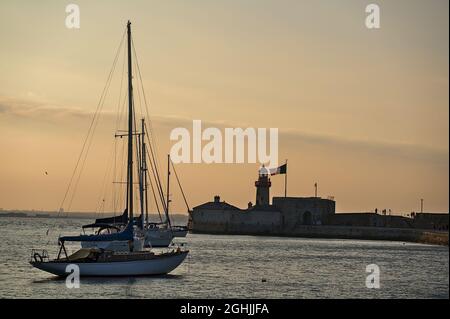 Dublin, Irland - 21. Juni 2021: Wunderschöne Abendansicht von Segelbooten, die in der Nähe des roten Leuchtturms am East Pier mit irischer Flagge im Hafen von Dun Laoghaire anlegen Stockfoto