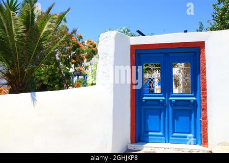 Eine blaue Tür in einer weißen Mauer mit einer Palme im traditionellen Dorf Megalochori, Santorini, Griechenland. Stockfoto