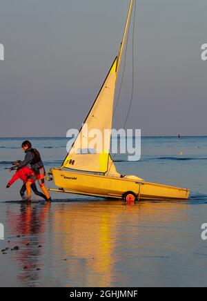 Segelboote/Schlauchboote werden bei Sonnenuntergang auf Trolleys/Anhängern am Littlehampton Beach, West Sussex, Großbritannien, eingezogen Stockfoto