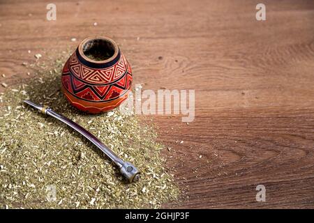 Traditionelle Mate aus Kalabash über einem Holztisch mit Yerba Mate darüber verstreut. Stockfoto