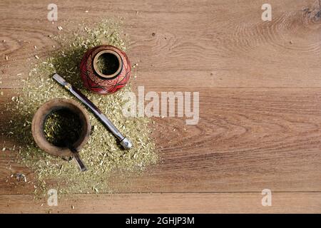 Zwei traditionelle Mate aus Kalabash auf einem Holztisch mit Yerba Mate, die darüber verstreut sind. Draufsicht. Stockfoto