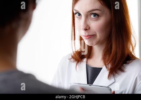 Frau, die einer Freundin oder Arbeitskollegin aufmerksam zuhört, in einer über die Schulter zugeschnittenen Ansicht ihres Gesichts mit weiten Augen und einem ernsthaften nachdenklichen Exp Stockfoto