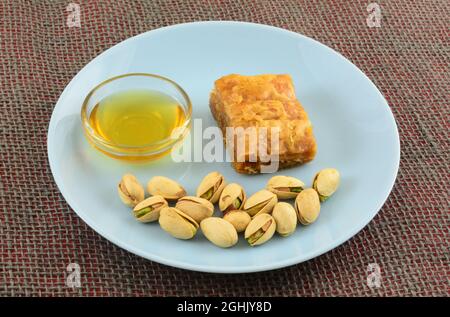 Stück Baklava mit Honig in Glasschale und Pistazien in Schalen auf blauem Snackteller Stockfoto