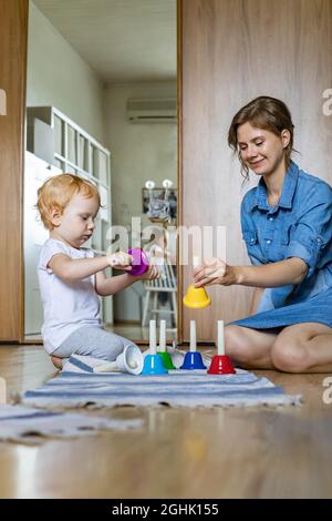 Junge Mutter und kleines Kleinkind spielen kindisch bunte Handglocken Musik zu Hause Stockfoto