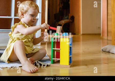 Happy girl Kleinkind Schlagen Holzhammer auf farbigen Kugeln frühe Entwicklung ökologischen Spielzeug Stockfoto