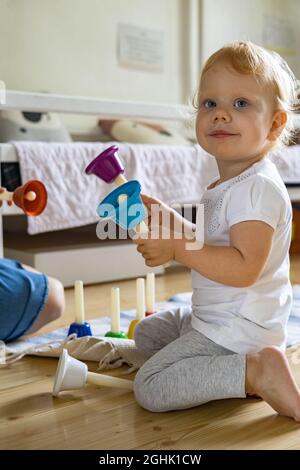 Lächelndes Baby, das farbige kindliche Handglocken spielt und die Melodie des Musikinstruments studiert Stockfoto