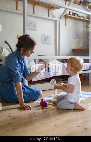 Junge Mutter und kleines Kleinkind spielen kindisch bunte Handglocken Musik zu Hause Stockfoto