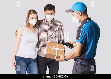 Ein Anlieferer in blauer Uniform brachte einem schönen jungen Paar ein Paket mit dem Handy in der Hand und allen Menschen, die einen Arzt trugen Stockfoto
