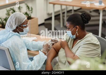Schwarze Frau in schützender Gesichtsmaske wird im Krankenhaus gegen Coronavirus geimpft Stockfoto