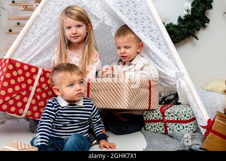 Glückliche Kinder sitzen zwischen Weihnachts-Geschenkboxen und Spielzeug in einem dekorierten Haus, glücklich Kindheit Konzept Stockfoto