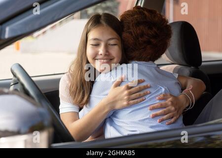 Nettes, fröhliches Mädchen und ihre Mutter umarmen sich im Auto, bevor die Tochter zur Schule geht Stockfoto