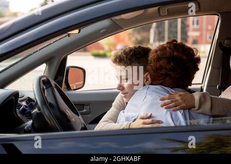 Der Schuljunge umarmt seine Mutter im Auto, bevor er morgens zur Schule geht Stockfoto