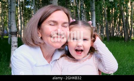 Fröhlich lachend zarte Großmutter spielt und umarmt ihre kleine 3-jährige Enkelin. Das Konzept der generationenübergreifenden Beziehungen, ein glücklicher Stockfoto