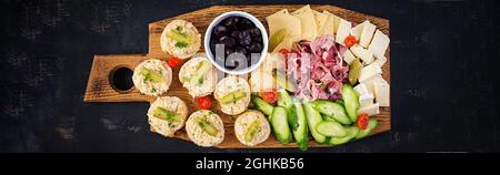 Antipasto-Catering-Platte mit Jamon, Käse, Canape und schwarzen Oliven auf einem Holzbrett. Draufsicht, Banner Stockfoto