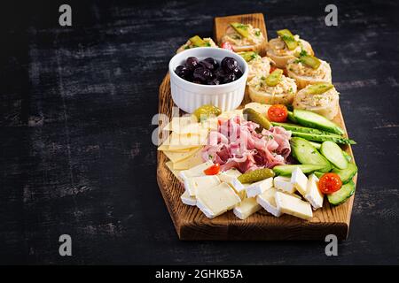 Antipasto-Catering-Platte mit Jamon, Käse, Canape und schwarzen Oliven auf einem Holzbrett. Draufsicht, Overhead Stockfoto