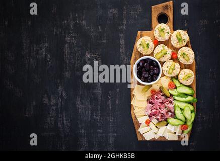 Antipasto-Catering-Platte mit Jamon, Käse, Canape und schwarzen Oliven auf einem Holzbrett. Draufsicht, Overhead Stockfoto