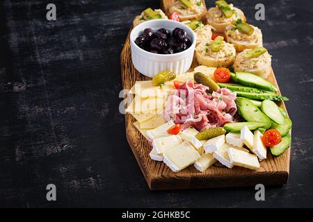 Antipasto-Catering-Platte mit Jamon, Käse, Canape und schwarzen Oliven auf einem Holzbrett. Draufsicht, Overhead Stockfoto