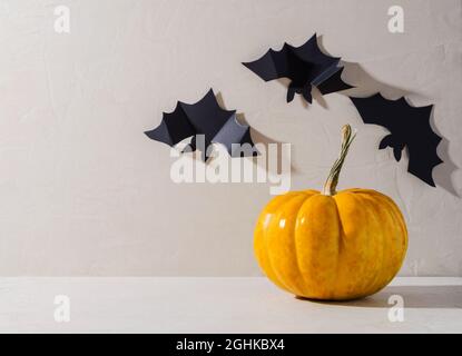 Minimalistischer Hintergrund von Halloween. Orangefarbener Kürbis und dekorative schwarze Fledermäuse auf beigem Hintergrund, Text kopieren Stockfoto