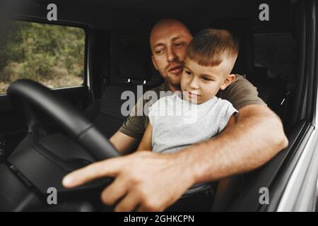 Vater lehrt den kleinen Sohn auf einer Autoreise zu fahren Stockfoto