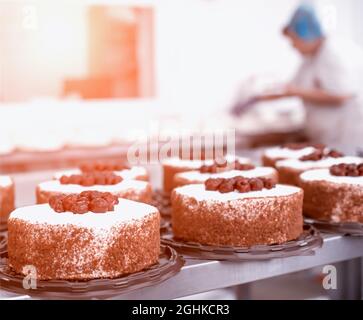 Konditorköchin Girl macht einen Kuchen aus frischen Keksbeeren und Sahne. Massenproduktion von Kuchen und Süßigkeiten, Süßwarenfabrik Stockfoto