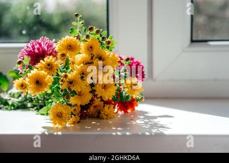 Schöner Herbststrauß mit gelben Astern und Chrysanthemen-Blüten auf Fensterbank Stockfoto