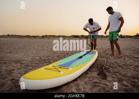 Junger Mann, der bei Sonnenaufgang am Strand Paddel aufbläht Stockfoto