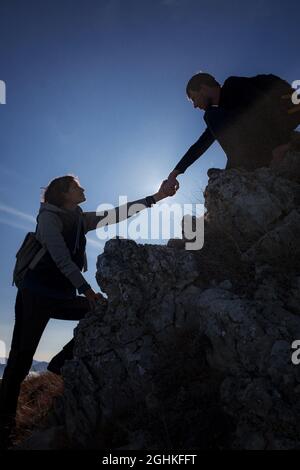 Hilfe- und Hilfekonzept. Silhouetten von zwei Menschen, die Berge besteigen und gegen den blauen Himmel helfen. Gehen Sie in den Wolken. Discovery Travel Direc Stockfoto