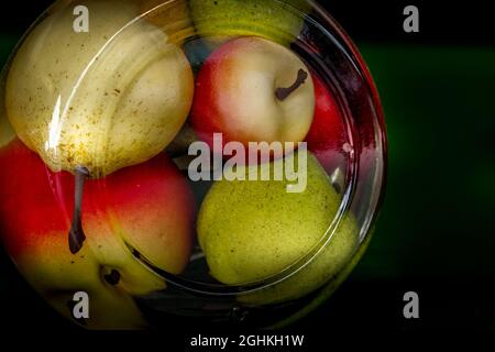 Konservierte Äpfel aus der Dose und Birne in einem großen Glas auf dunklem Grund Stockfoto